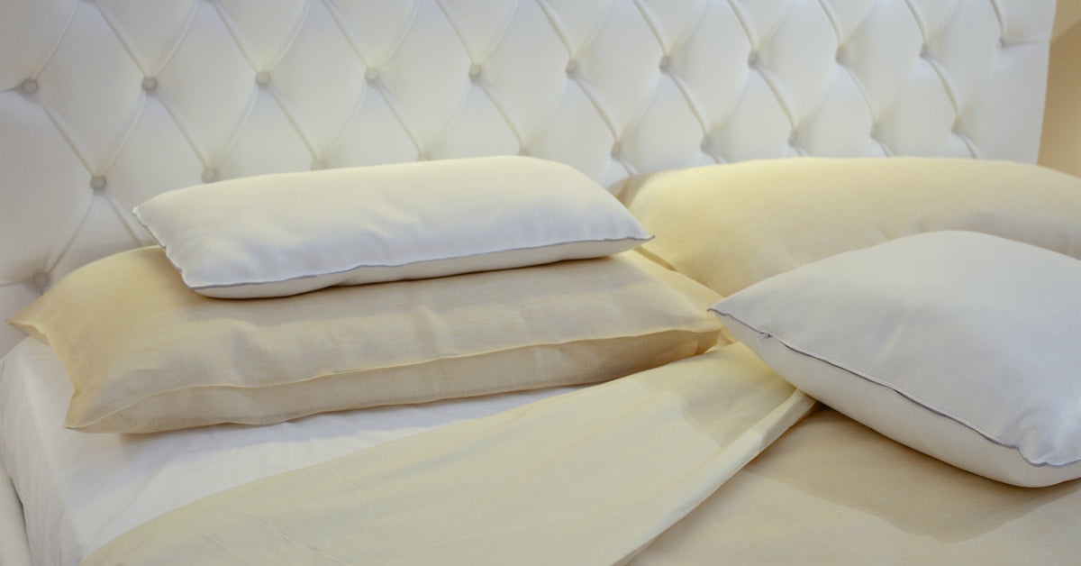 Stacked ivory and white pillows on a bed with a tufted headboard
