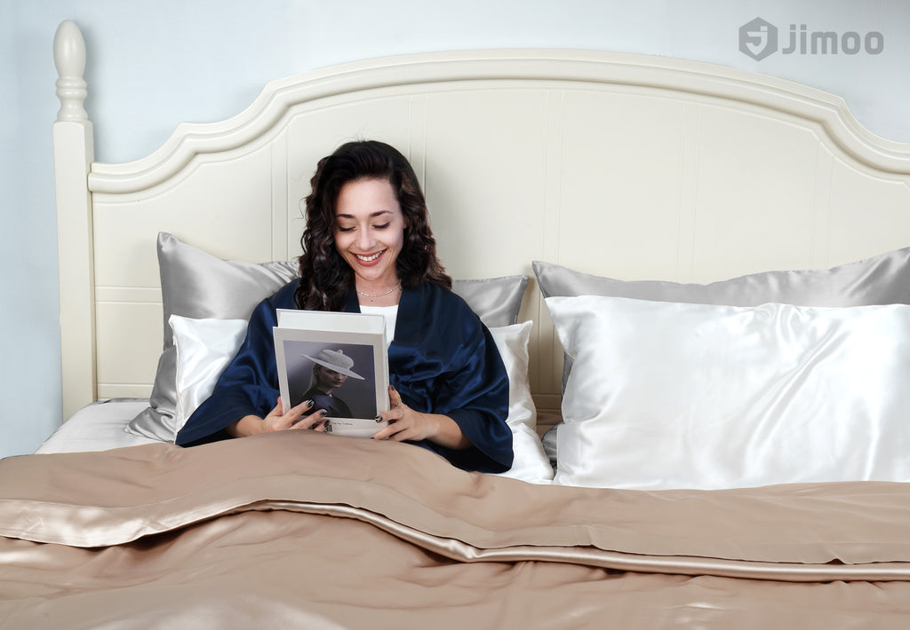 Woman reading in bed surrounded by lustrous silk pillowcases, enjoying a relaxed morning.
